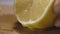 Squeezing lemon juice from a lemon half. Action. Close up of female hand getting lemon juice on a wooden board surface.