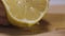 Squeezing lemon juice from a lemon half. Action. Close up of female hand getting lemon juice on a wooden board surface.