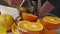 Squeezing an orange fruit with a manual press, close view, making a glass of fresh. Fresh oranges on a wooden table, whole and sli
