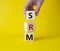 SRM - Sustainability Risk Management symbol. Wooden cubes with word SRM. Businessman hand. Beautiful yellow background. Business