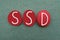 SSD, Shared Delusional Disorder, logo type composed with red colored stone letters over green sand