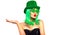 St. Patrick`s Day leprechaun model girl in green hat, funny clover sunglasses holding product, pointing hand, isolated on white