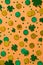 St. Patrick`s day pattern made of gold coins, shamrock clover leaves and confetti on orange background. Flat lay, top view,