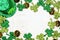 St Patricks Day frame of green shamrocks, gold coins and leprechaun hat, top view over a white wood background with copy space