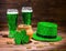 St Patricks day with glasses of green beer, leaf clover, leprechaun hat and pot full gold coins on vintage wooden