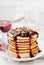 Stack of american pancakes or fritters with blackcurrant jam in plate on white table