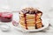 Stack of american pancakes or fritters with blackcurrant jam in plate on white table