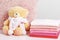 A stack of baby clothes and a teddy bear on a pink table. Gray wall background