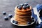 Stack of baked american pancakes or fritters with blueberries and honey syrup on rustic black table. Delicious dessert.
