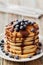 Stack of baked pancakes or fritters with chocolate sauce and frozen blueberries in a white plate