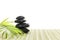 Stack of black basalt balancing stones with green leaf on bamboo mat, on white background.