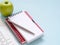 Stack blank notebook with pen and apple, the keyboard on the blue workplace desk table.