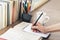 Stack of books education background, female hand makes notes in open notebook. Glasses, pens and pencils in holder, cup of tea