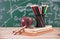 A stack of books in front of a blackboard full of mathematical formulas, a red apple, a magnifying glass and a pen holder filled w