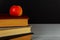 Stack of books with a red apple and a clean blackboard