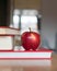 A stack of books in red covers and a red apple against the morning window. A metaphorical image of a good start to the day and