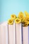 A stack of books with spring yellow daffodils flowers on aqua color background, copy space
