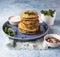 Stack of broccoli or spinach pancakes with yoghurt or cream sour dressing and microgreen, blue background. Vegetarian fritters.