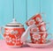 A stack of ceramic retro cups with red patternsand teapot on a pink wooden table against a blue wooden wall background