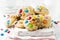 Stack of children cookies with colorful chocolate candies in a sugar glaze on a white light wooden background. Selective focus