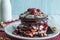 Stack of chocolate pancakes topped wtih cherry and walnuts, sprinkled with powdered sugar and drizzled with maple syrup. Gourmet B