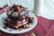 Stack of chocolate pancakes topped wtih cherry and walnuts, sprinkled with powdered sugar and drizzled with maple syrup. Gourmet B