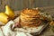 A stack of classic American pancakes on a light wooden board, two pears in the backdrop, a sprig of sea buckthorn on the side, and
