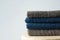 Stack of clean folded navy blue beige terry towels on wooden char gray wall background. Laundry spa wellness cleanliness concept
