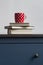 stack of closed books with tea cup on top on blue chest of drawers