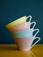 Stack of colorful vintage tea cups on yellow table against petrol background. Afternoon tea party. Vertical.