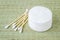 Stack of cotton pads and heap of wood stick cotton buds on a background of rough wicker mat made of bast fibers. Plastic free