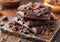 Stack of dark broken chocolate bar pieces with cocoa on table.Macro.AI Generative