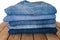 A stack of different pairs of blue jeans on a wooden table . Always in trend