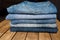 A stack of different pairs of blue jeans on a wooden table . Always in trend