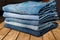 A stack of different pairs of blue jeans on a wooden table . Always in trend