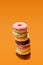 Stack of donuts on orange background including chocolate frosting, topping, coconut and frosting
