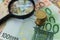 Stack of Euro coins on pile of banknotes with magnifying glass a