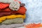 Stack of folded warm knitted women`s sweaters, scarf, hat with pompom in warm colors and autumn leaves. Copy space