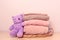Stack of folded wool knitted sweaters or pullovers in pink pastel colors on table with soft toy Taddy bear