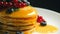 Stack of fresh fluffy pancakes decorated on top with forest berries rotating on plate and pouring honey syrup. Delicious