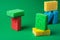 Stack geometric blocks construction abstract sponges in red, yellow, blue colors, on green paper background, copy space