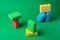 Stack geometric blocks construction abstract sponges in red, yellow, blue colors, on green paper background, copy space