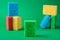 Stack geometric blocks construction abstract sponges in red, yellow, blue colors, on green paper background, copy space