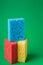 Stack geometric blocks construction abstract sponges in red, yellow, blue colors, on green paper background, copy space