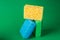 Stack geometric blocks construction abstract sponges in yellow, blue, green colors, on green paper background, copy space