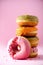 Stack of glazed colorful assorted donuts with sprinkles on pink background. Copy space. Sweet doughnuts for kids