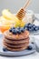 Stack of healthy oatmeal banana pancakes garnished with blueberry and honey, honey is flowing down from honey dipper or spoon, on