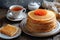 Stack homemade thin pancakes decorated with red caviar on white plate and cup of tea on wooden background, festive dish