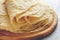 Stack of homemade wheat flour tortilla wraps on wooden cutting board.