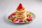 Stack of hot flapjacks served with fresh strawberries and kiwi on white wooden table